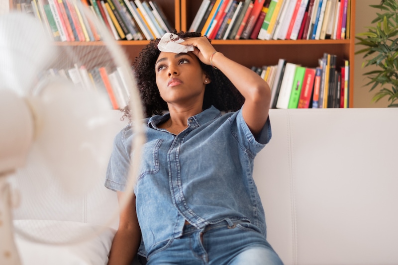 Common AC Problems - Black woman sweating and trying to refresh at home.